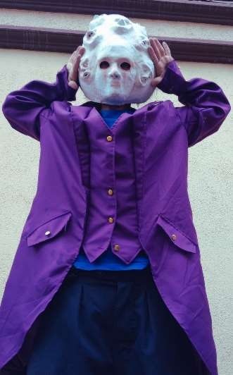 Persona que lleva una máscara blanca con agujeros para los ojos, abrigo morado y orejas que cubren.